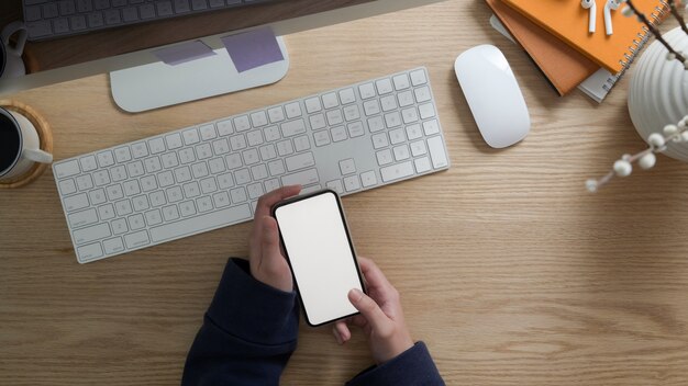 Draufsicht des Freiberuflers, der leeres Bildschirmtelefon beim Sitzen am Arbeitsplatz hält