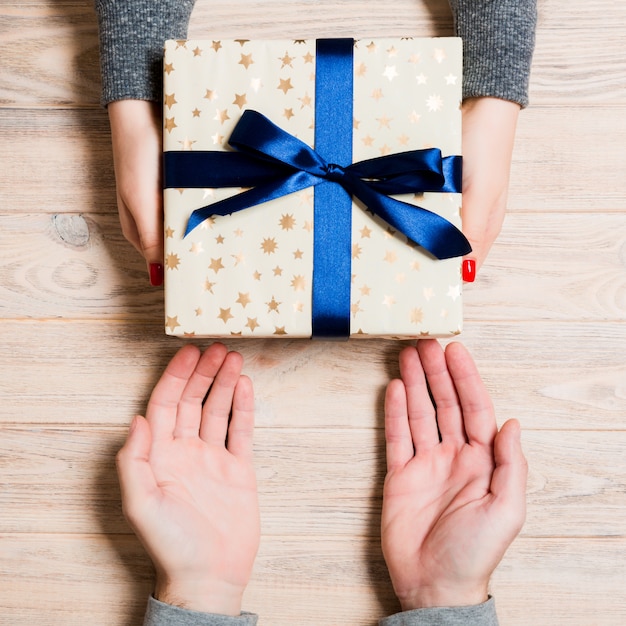 Draufsicht des Gebens und des Empfangens eines Geschenks auf Holztisch. Ein Mann und eine Frau, die Geschenk in den Händen halten. Abschluss oben des festlichen Konzeptes