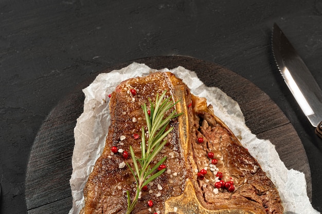 Draufsicht des gegrillten T-Bone-Steaks mit Gewürzen auf schwarzem Tisch