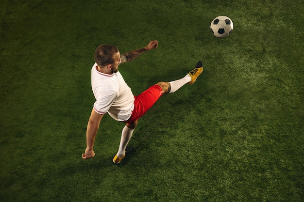 Draufsicht des kaukasischen Fußball- oder Fußballspielers auf grünem Hintergrund des Grases. Junges männliches sportliches Modelltraining, übend. Ball treten, angreifen, fangen. Konzept des Sports, des Wettbewerbs, des Gewinnens.