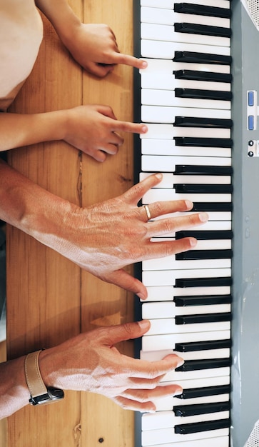 Draufsicht des Klaviers und Hände des Kindes, das mit dem Vater zu Hause lernt, spielt oder sich zusammenschließt Entwicklungserziehung oder Eltern, die dem Kind beibringen, wie man Musikinstrumente spielt, akustische oder elektrische Tastatur