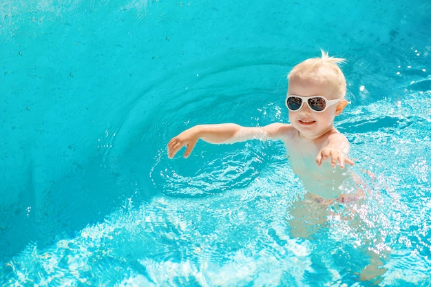 Draufsicht des kleinen Mädchens, das im Pool mit blauem Wasser schwimmt.