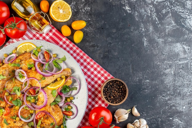 Draufsicht des köstlichen abendessens gebratenes hühnergericht mit verschiedenen gewürzen und nahrungsmitteln tomaten mit stielen pfeffer zwiebeln knoblauch gefallene ölflasche zitrone auf der rechten seite auf dunklem hintergrund
