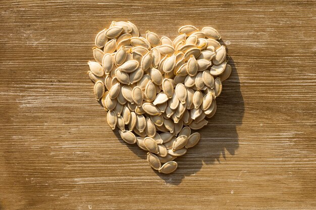 Draufsicht des Kürbises der rohen Samen in Form des Herzens auf dem hölzernen Hintergrund Beschneidungspfad eingeschlossen. Konzept gesund für das Herz.