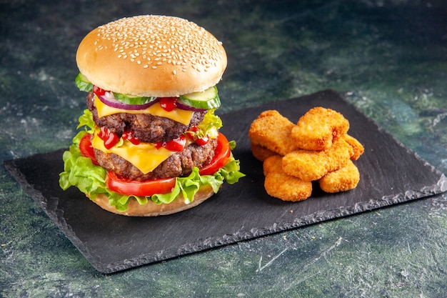 Draufsicht des leckeren Fleischsandwiches mit Tomatengrün auf dunklem Farbtablett und Hühnernuggets auf schwarzer Oberfläche