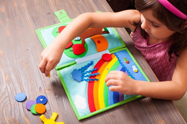 Draufsicht des Mädchens spielt mit einem Textilbuch auf dem Holztisch Das Mädchen ordnet Kreise nach Regenbogenfarben im Buch an