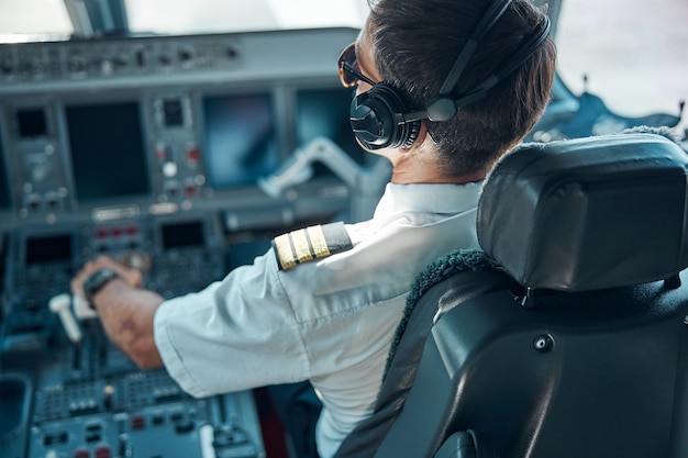 Draufsicht des Mannes in Luftfahrtuniform und Kopfhörern, die beim Start am Steuer sitzen und das Ruder schalten