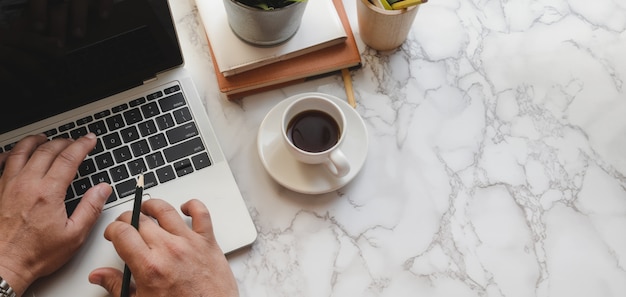 Foto draufsicht des mannes schreibend auf laptop-computer an modernem stilvollem arbeitsplatz auf marmortabelle