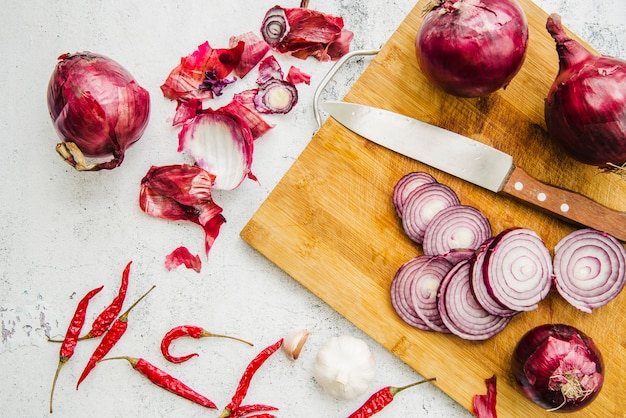 Foto draufsicht des messers; in scheiben geschnittene zwiebel auf schneidebrett mit roten chili und knoblauch