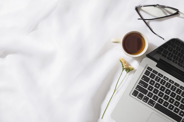 Draufsicht des Morgen-Tees im Voile-Stoffhintergrund mit einem Laptop, einer Tasse Tee, Gläsern und einer Blume mit Raum für Text