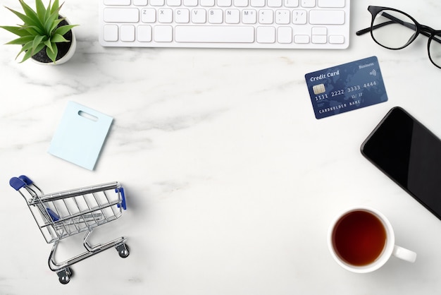 Draufsicht des Online-Einkaufskonzepts mit Kreditkarte, Smartphone und Computer lokalisiert auf weißem Tischhintergrund des Büromarmors.