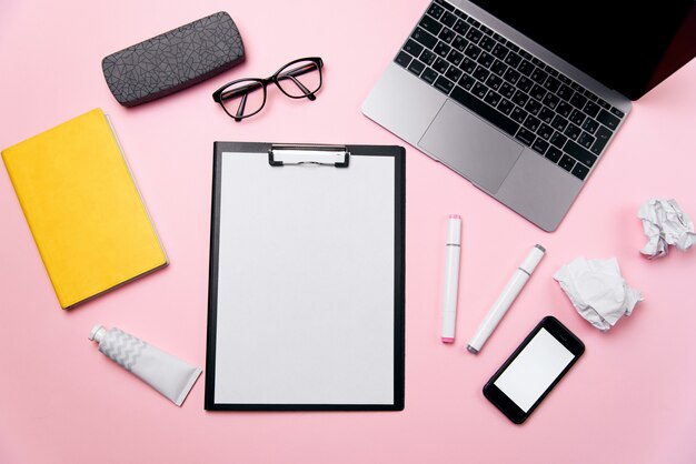 Draufsicht des rosa Büroschreibtischs der Frau mit sauberem Blatt Papier mit freiem Kopierraum, Laptop, Telefon mit leerem weißen Bildschirm, einer Creme, Brille und liefert Hintergrund.