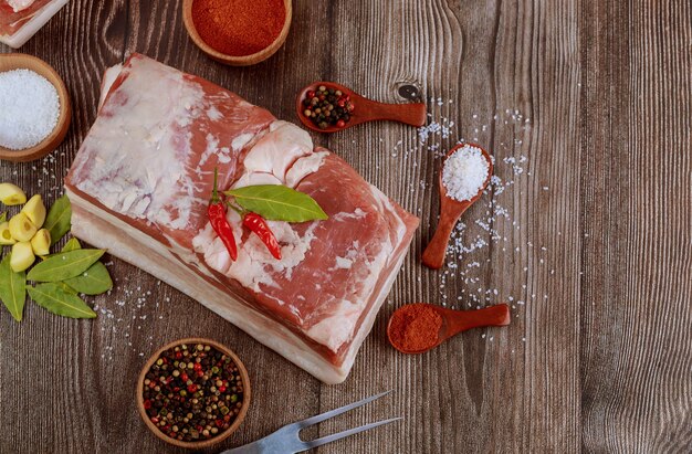 Draufsicht des Stückes des rohen Schweinebauches mit Salz und rotem Paprika auf rustikalem Holztisch