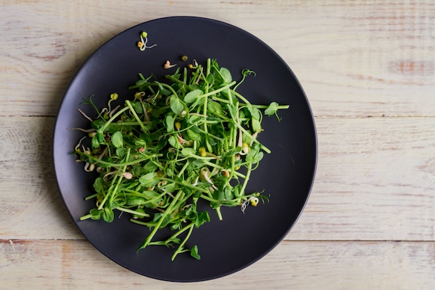 Draufsicht des veganen gesunden Salats gemacht von den mikrogrünen Erbsensprossen der Erbsen und der gekeimten Bohnen auf Holzwand