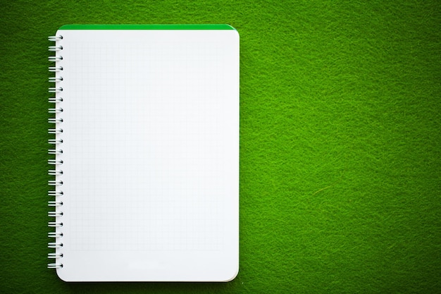 Draufsicht des weißen Notizbuches auf grünem Tisch.