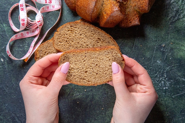 Draufsicht dunkle Brotlaibe mit weiblichen Händen auf dunklem Schreibtisch