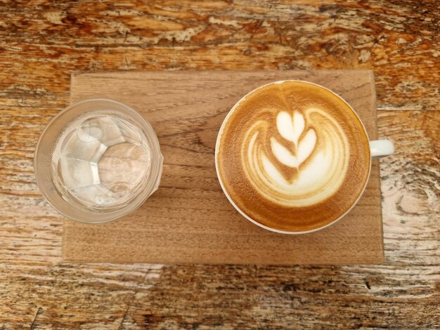 Draufsicht eine Tasse Latte Art Kaffee mit Trinkwasser auf einer Holzplatte