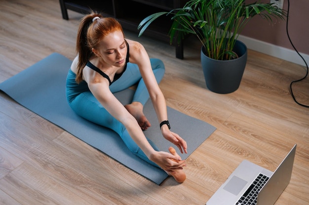 Draufsicht einer flexiblen rothaarigen jungen frau, die beim dehnübungen auf einer yogamatte trainiert