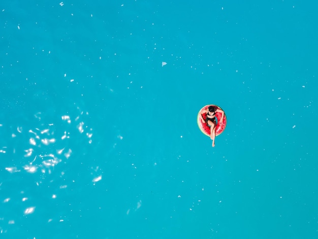 Draufsicht einer Frau, die auf einem aufblasbaren Ring im blauen Meerwasser schwimmt