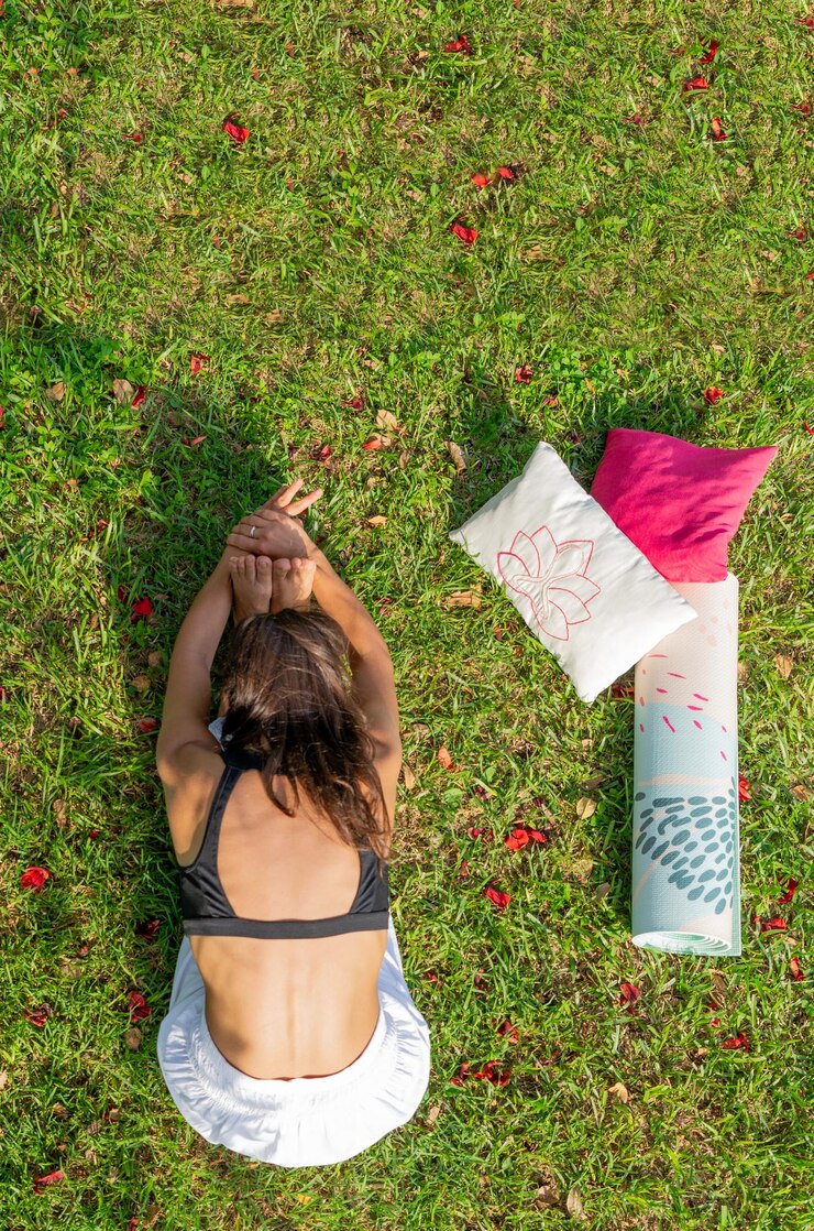 Draufsicht einer jungen Frau, die Yoga auf einer grünen Wiese praktiziert und sich nach vorne beugtVertikalbild