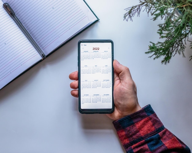 Draufsicht einer männlichen Hand, die ein Mobiltelefon mit einem Kalender für 2023 hält