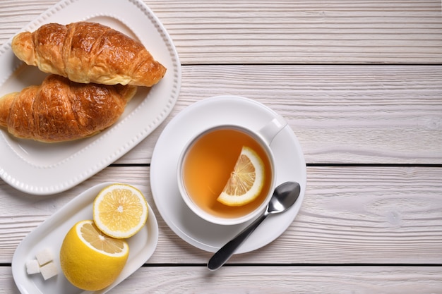 Draufsicht einer Tasse Tee mit Zitrone und Croissants auf weißem Tisch