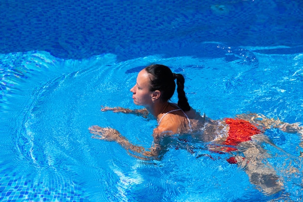 Draufsicht eines gebräunten Mädchens, weiblich, Modell in einem roten Badeanzug, Schwimmen im blauen Wasser des Pools.