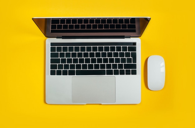 Draufsicht eines Laptops neben einer weißen Maus auf Gelb