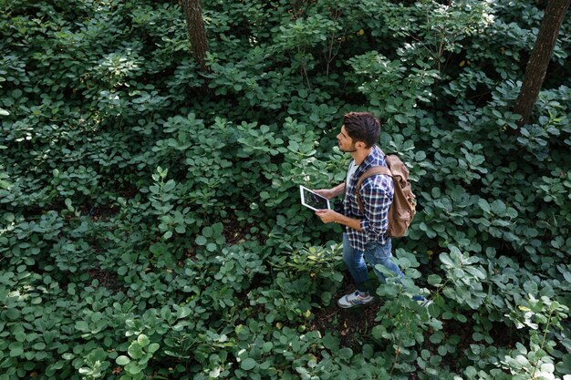 Draufsicht eines Mannes im Hemd, der mit Tablet, Fernglas und Rucksack im Wald spaziert wood