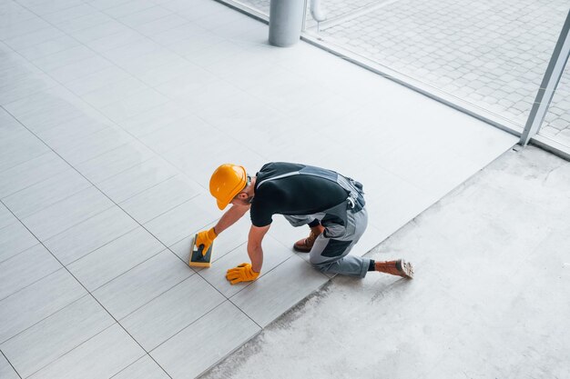 Draufsicht eines Mannes in grauer Uniform, der tagsüber in einem modernen großen Büro eine Platte installiert