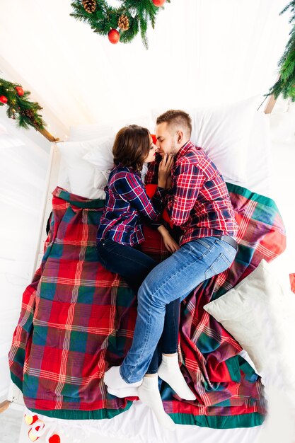 Draufsicht eines Paares, das auf einem Bett mit Weihnachtsschmuck liegt und sich küssen möchte