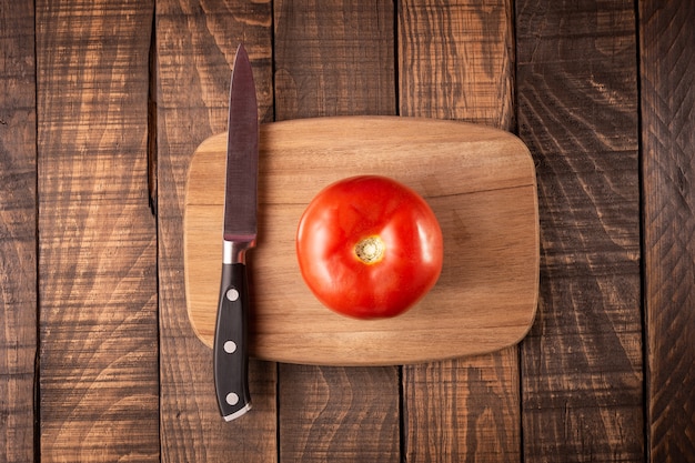 Draufsicht eines Schneidebretts mit einer Tomate auf einem Holztisch