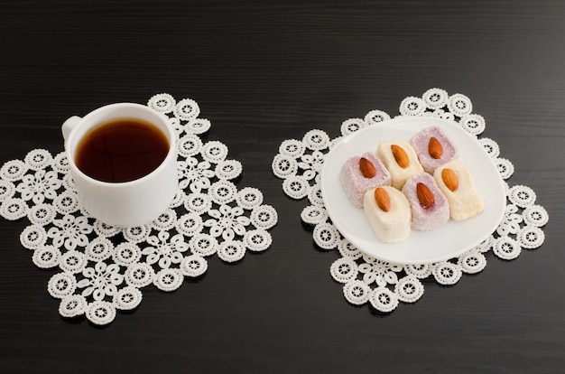 Draufsicht eines Tasse Kaffees und der bunten türkischen Freude mit Mandeln auf der schwarzen Tabelle der Spitzenservietten