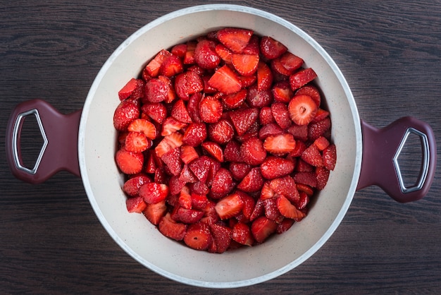 Draufsicht eines Topfes mit frischen Erdbeeren schnitt die Stücke ein, die für ein Erdbeermarmeladenkochen vorbereitet wurden.