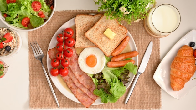 Draufsicht Englisches Frühstücksset mit Ei, Schinken, Würstchen, Toast, Croissant, Milch und Salat auf dem Tisch