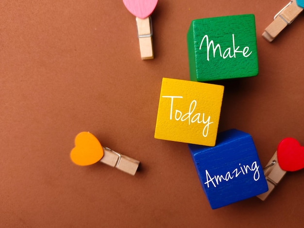 Draufsicht farbiger Block und Holzclips mit Text Make Today Amazing auf braunem Hintergrund