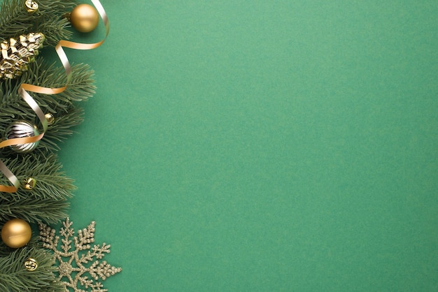 Draufsicht Foto von goldenen und silbernen Weihnachtsbaumkugeln Spielzeugkegel kleine Glocken Schneeflocke und Serpentin auf Kiefernzweigen auf isoliertem grünem Hintergrund mit Leerzeichen