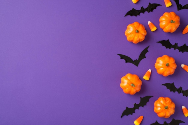 Draufsicht Foto von Halloween-Dekorationen kleine Kürbisse Candy Corn und Fledermäuse Silhouetten auf isoliertem violettem Hintergrund mit Copyspace