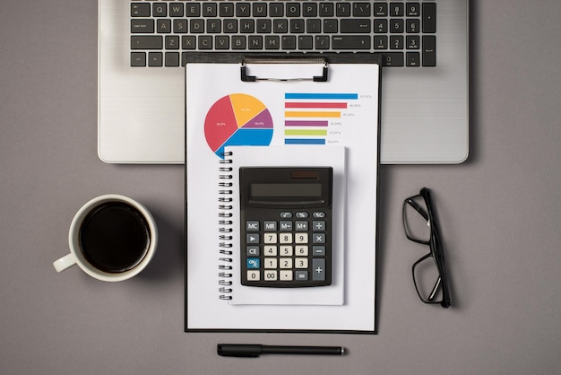 Draufsicht Foto von Laptop Tastatur Brille Stift Tasse Kaffee und Taschenrechner auf Notizbuch und Klemmbrettordner mit Kreisdiagramm auf isoliertem grauem Hintergrund