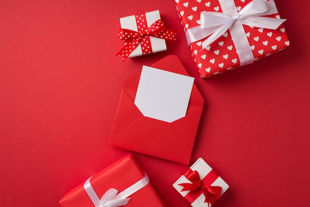 Draufsicht Foto von St. Valentinstag Dekorationen roter offener Umschlag mit Papierblatt rote und weiße Geschenkboxen auf isoliertem rotem Hintergrund mit Leerzeichen