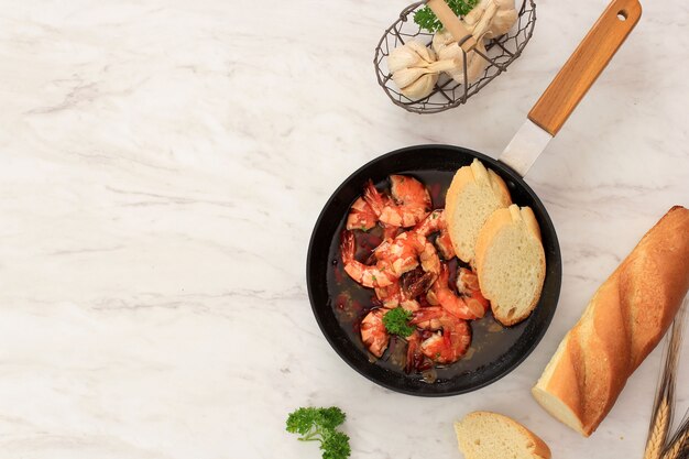 Draufsicht Gambas al aJillo. Garnelen-Scampi auf einer Pfanne. Traditionelle spanische Tapa mit Garnelen in Olivenöl mit Knoblauch und Chili gekocht. Serviert mit Baguette, Platz für Text kopieren