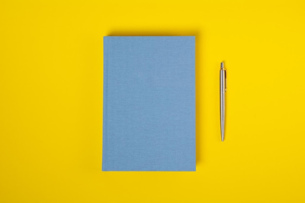 Draufsicht geschlossenes blaues Notizbuch und Stift über gelbem Hintergrund mit Kopienraum