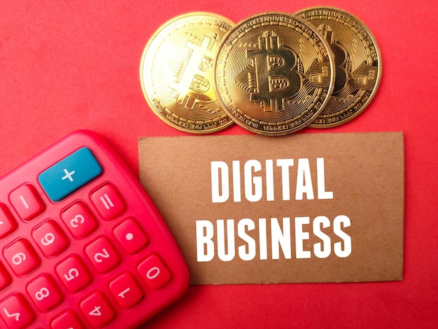 Draufsicht goldenes Bitcoin und Taschenrechner mit Text DIGITAL BUSINESS auf blauem Hintergrund