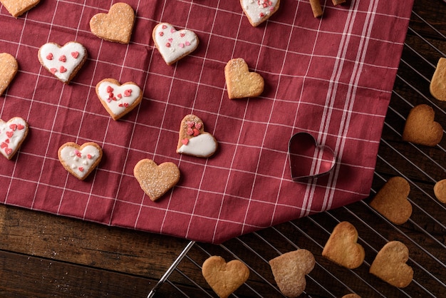 Draufsicht hausgemachte Kekse Herzen mit weißem Zuckerguss und Gebäck auf kastanienbraunem Handtuch und Metallgitter für Valentinstag