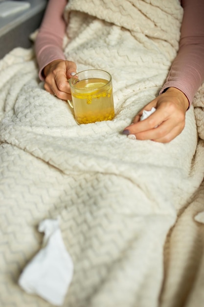 Draufsicht Kranke Frau, die eine Tasse warmen Sanddorntee hält und zu Hause unter einer Decke sitzt, kranke Dame, natürliche Heilmittel für Erkältungen, Konzept der Naturmedizin.