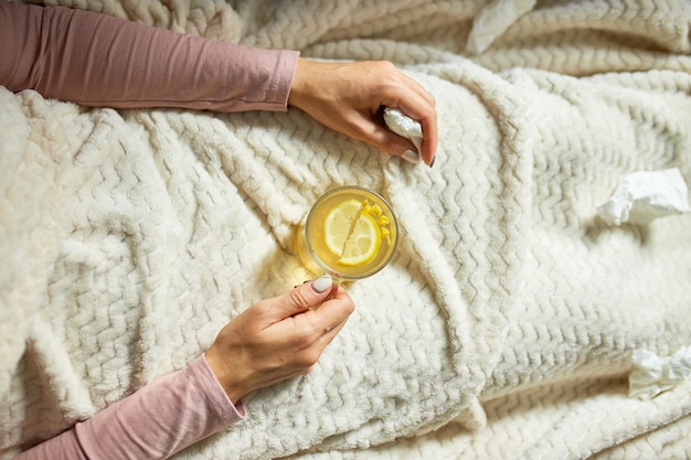 Draufsicht Kranke Frau, die eine Tasse warmen Sanddorntee hält und zu Hause unter einer Decke sitzt, kranke Dame, natürliche Heilmittel für Erkältungen, Konzept der Naturmedizin.