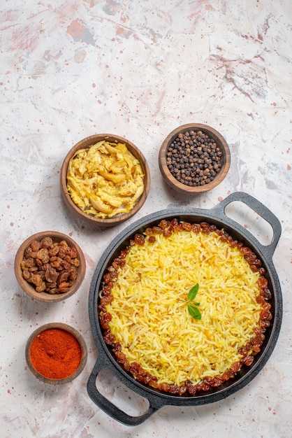 Draufsicht leckerer Plov in großer Pfanne Huhn trockene Trauben schwarze und rote Paprika in Schalen auf dem Tisch