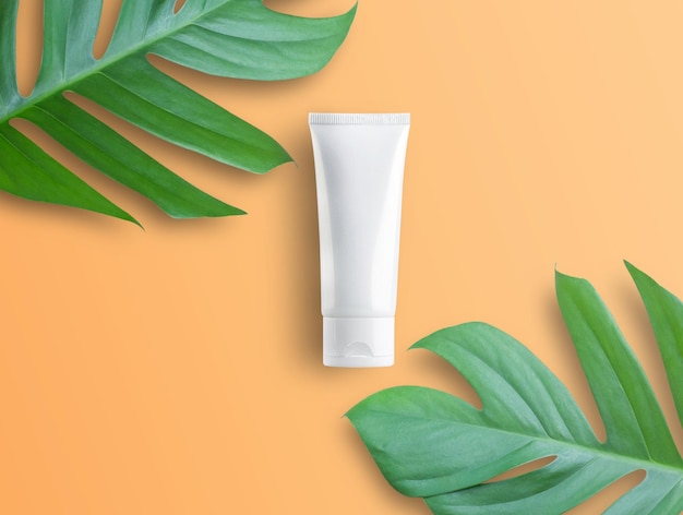 Draufsicht mit weißen Kosmetikprodukten und grünen Blättern auf orangefarbenem Hintergrund