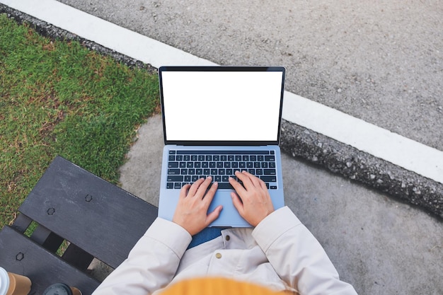 Draufsicht-Mockup-Bild einer Frau, die einen Laptop-Computer mit einem leeren weißen Desktop-Bildschirm im Freien hält und verwendet