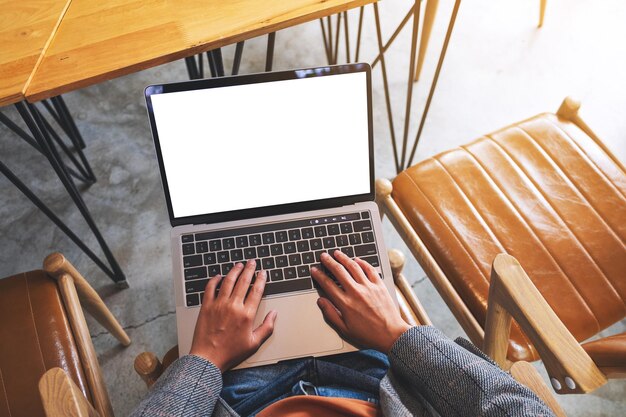 Draufsicht-Mockup-Bild einer Frau, die einen Laptop-Computer mit leerem weißem Desktop-Bildschirm verwendet und darauf tippt